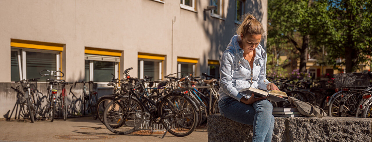 Lesende sitzt vor den Fahrradständern an Campus I der KH Freiburg