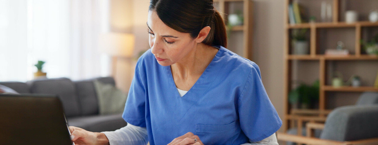 A woman, a medical professional, is working on a laptop.