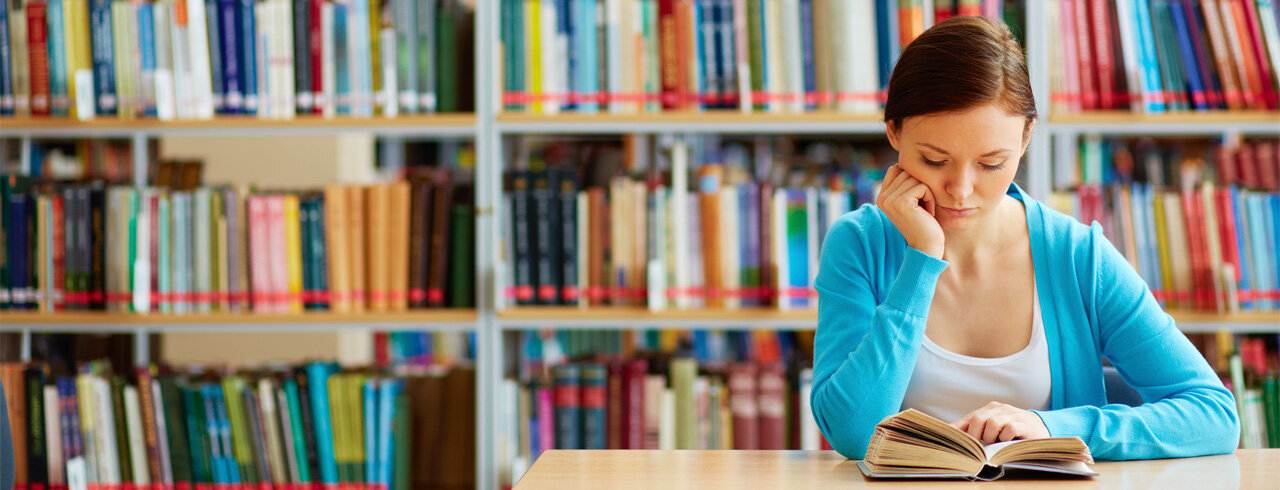 Studierende sitzt in einer Bibliothek und liest ein Buch