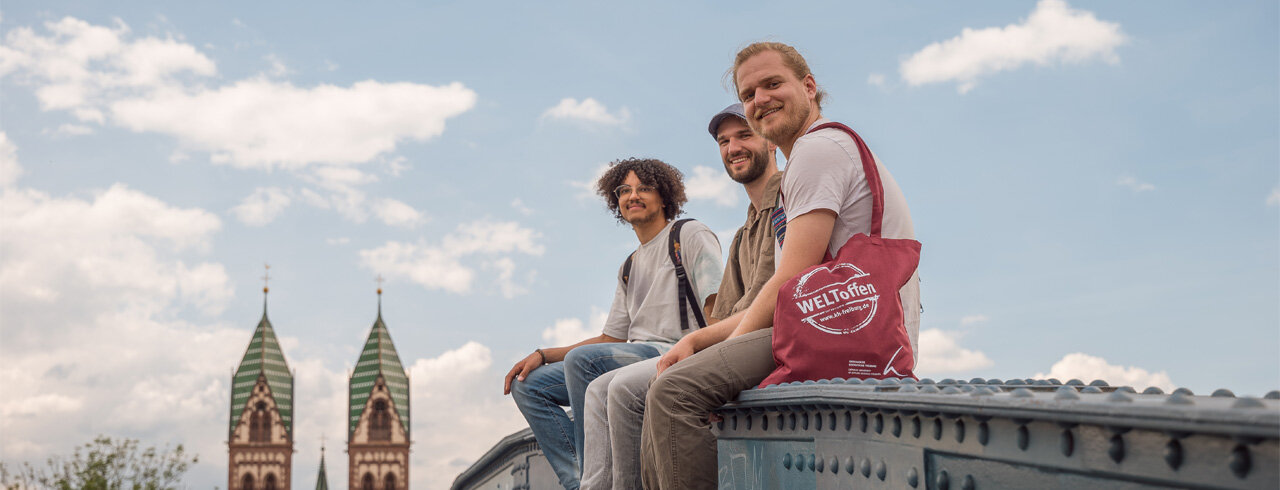 drei Studierende sitzen auf der Wiwilli-Brücke in Freiburg