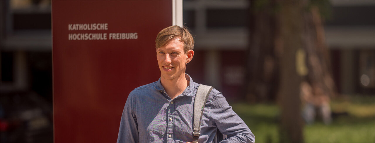 Zielstrebig schauender, junger Mann vor den Campusgebäuden der KH Freiburg