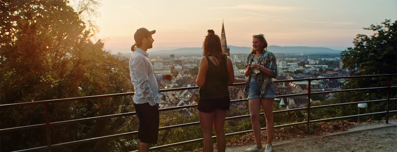 Studierende auf dem Schlossberg Freiburg. Die Sonne geht im Hintergrund hinter dem Münster unter